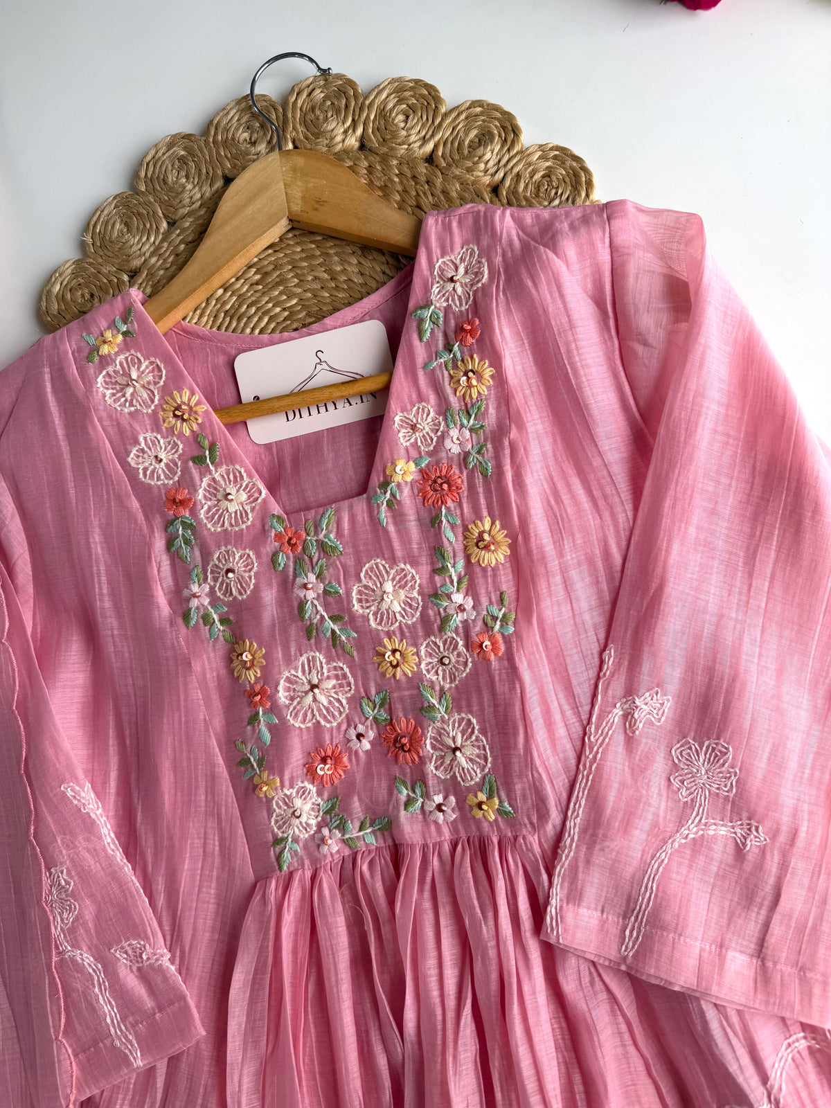 Pink embroidered dress on a hanger against a white wall